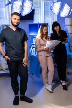 Hastane personeli takım çalışması. Üç sağlık uzmanı, iyi aydınlatılmış bir hastane odasında hasta dosyalarını tartışıyorlar. İşlerine odaklanıyorlar..