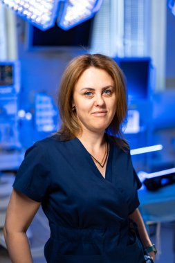 Modern ameliyathane ortamında bir cerrah. Bir tıp uzmanı, mavi ışıkla aydınlatılmış modern bir ameliyathanede güvenle poz verir..