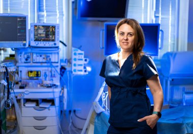 Doktor hastane biriminde. Bir sağlık çalışanı, gelişmiş tıbbi ekipman ve monitörlerle dolu modern bir hastane odasında güven içinde poz verir..