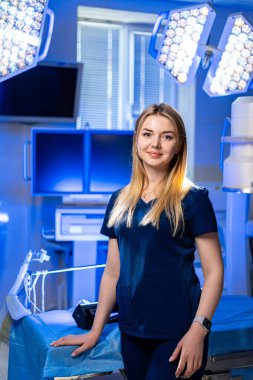 Ameliyathanede bir cerrah. Bir sağlık çalışanı, modern tıbbi ekipman ve aydınlatma ile çevrili, parlak bir ameliyathanede güven içinde duruyor..