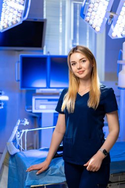 Ameliyathanede genç bir cerrah. Kendine güvenen bir kadın sağlık çalışanı modern bir cerrahi süitte gelişmiş ekipman ve parlak ışıklandırmayla duruyor..