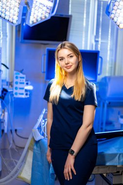 Genç doktor ameliyatta. Tıbbi önlüklü genç bir kadın, parlak ışıklarla aydınlatılmış modern bir ameliyathanede güvenle duruyor..