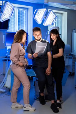 Doktorlar hasta bakımını tartışıyor. Hastanede, iki çalışan hasta tedavisi hakkında bir meslektaşlarına danışır ve belgeleri incelerler..