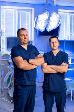 Hastane sağlık personeli. İki doktor, iyi aydınlatılmış bir hastane odasında, gelişmiş tıbbi ekipmanlarla hasta bakımına hazır bekliyor..