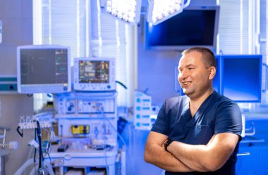 Klinikteki gülümseyen doktor. Bir doktor, ileri teknoloji ile çevrili, iyi donanımlı bir tıp odasında kollarını kavuşturarak güvenle durur..