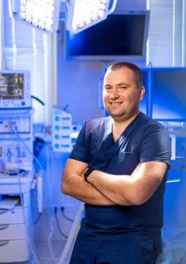 Klinikteki gülümseyen cerrah. Kendine güvenen bir sağlık uzmanı gelişmiş ekipmanlarla dolu yüksek teknolojili bir ameliyathanede duruyor..