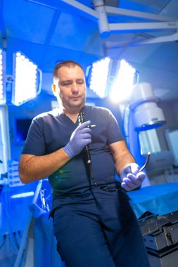 Cerrah ameliyata hazırlanıyor. Ameliyat önlüğü giyen bir cerrah, cerrahi aletleri parlak, yüksek teknolojili bir ameliyathanede tutuyor ve tıbbi bir prosedüre hazırlanıyor..