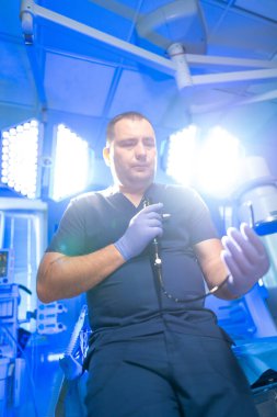 Doktor prosedüre hazır. Koyu renk önlüklü bir tıp uzmanı aydınlık bir ameliyathanede endoskop hazırlıyor..