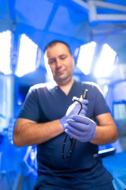 Cerrah aletleri ayarlar. Eldiven giyen bir tıp uzmanı ameliyat için hazırlanan parlak bir ameliyathanede cerrahi aletler bulundurur..