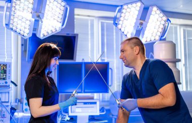 Cerrahlar ameliyata hazırlanır. Önlüklü iki sağlık çalışanı, parlak ve modern bir ameliyathanede ameliyatları tartışıyor..