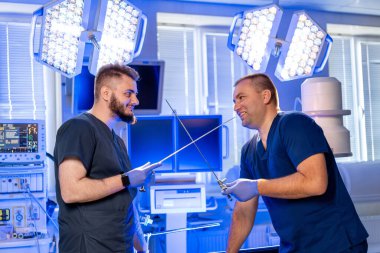 Cerrahlar ameliyattan önce sohbet ediyorlar. İki cerrah ameliyathanede aletleriyle yaklaşan bir prosedüre hazırlanırken aynı kahkahayı atıyorlar..