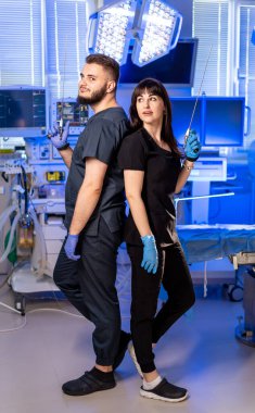 Sağlık uzmanları tarafından ameliyat hazırlığı. İki sağlık çalışanı, ellerinde cerrahi aletlerle, parlak bir cerrahi odada sırt sırta dururlar..