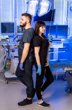 Cerrahi ekipmanlı cerrahlar. İki sağlık uzmanı modern bir ameliyathanede eldiven takarak sırt sırta cerrahi aletler kullanırlar..