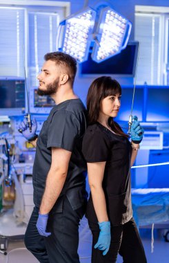 Cerrahi ortamdaki doktorlar. İki sağlık çalışanı sırt sırta bir ameliyathanede aletlerini ve kendine güvenen tavırlarını sergiliyorlar..