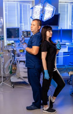 Doktorlar ameliyathanede. İki sağlık çalışanı, modern bir ameliyathanede parlak ışıkları olan cerrahi aletlerle sırt sırta dururlar..