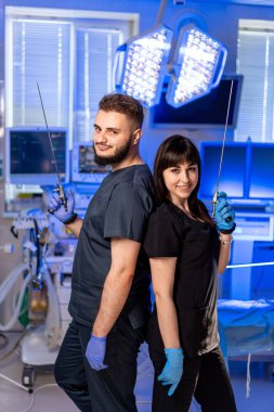 Hastanede oyun oynayan sağlık görevlileri. İki sağlık çalışanı sırt sırta verip modern hastane ameliyathane ortamında aletleri tutuyorlar..