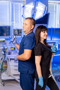 Hastanede kendine güvenen tıbbi personel var. İki tıp uzmanı bir hastanede sırt sırta dururlar, ellerinde cerrahi aletler ve takım çalışmalarını gösterirler..