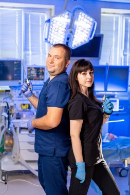 Tıp uzmanları ameliyata hazır. İki sağlık çalışanı arka arkaya parlak bir cerrahi odasında, ellerinde aletlerle ameliyata hazırlar..