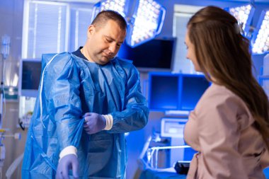 Hastane prosedürü hazırlığı. Mavi önlüklü bir tıp uzmanı ameliyat için hazırlanırken bir hasta hastane odasında gözlem yapıyor..