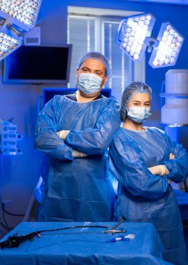 Tıp uzmanları ameliyata hazır. Cerrahi kıyafetli iki tıp uzmanı modern bir ameliyathanede ameliyata hazır bekliyor..