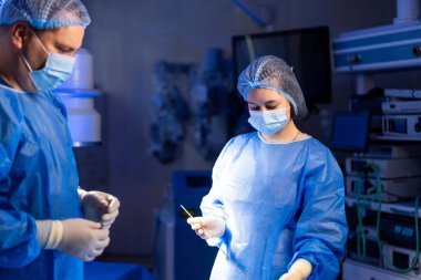 Cerrahlar steril odada ameliyat yaparlar. Mavi önlüklü ve maskeli iki cerrah modern bir ameliyathanede cerrahi müdahaleye odaklanıyor..