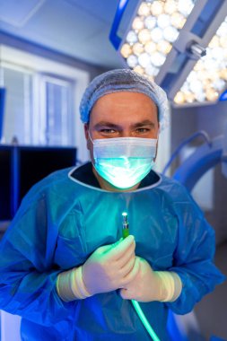 Cerrah ameliyata hazırlanıyor. Bir ameliyathanede cerrahi aletler ve parlayan ameliyat ışıklarıyla hazır yetenekli bir tıp uzmanı duruyor..