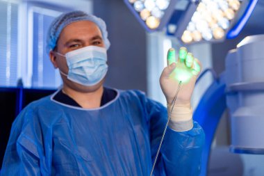 İleri teknoloji kullanan bir cerrah. Cerrahi giysiler içinde bir sağlık uzmanı ameliyathanede yenilikleri ön plana çıkaran parıldayan bir cihaz gösteriyor..