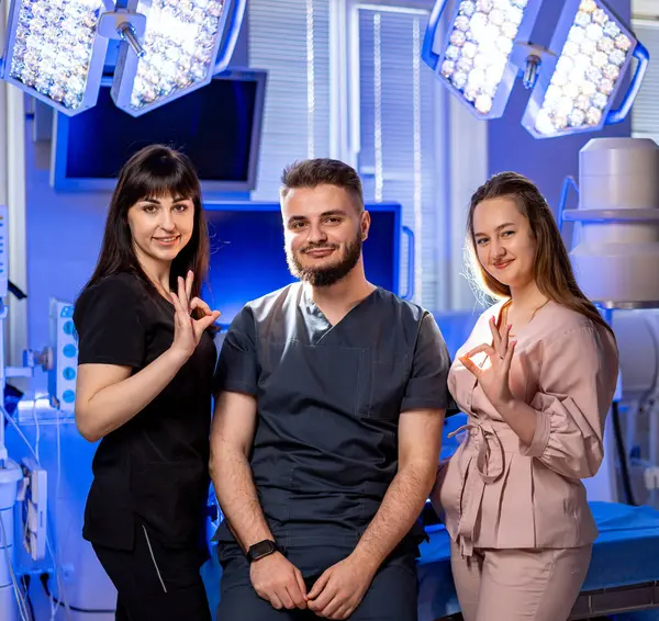 Modern bir klinikteki doktorlar. Üç sağlık çalışanı, iyi aydınlatılmış bir klinikte, önlükleri ve kıyafetleriyle güvenle sırıtarak bir arada duruyorlar..