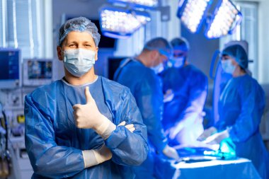 Cerrahlar onaylar! Meslektaşları arka planda ameliyat yaparken kendine güvenen bir cerrah ameliyathanede duruyor..