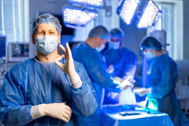 Ameliyat başarıyla tamamlandı. Cerrahi kıyafetli bir tıbbi ekip ameliyathanede işbirliği yaparken, bir üye onay veriyor..