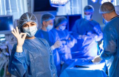 Cerrahlar ameliyathanede. Önlüklü bir grup cerrah, iyi aydınlatılmış bir ameliyathanede karmaşık bir prosedür üzerinde çalışıyorlar..