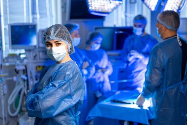 Ya da sağlık uzmanları. Sağlık uzmanlarından oluşan bir ekip, parlak ışıklandırılmış bir ameliyathanede birlikte çalışarak cerrahi bir prosedüre odaklanıyor..