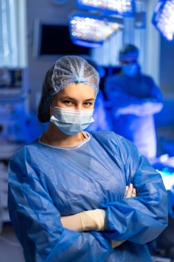 Cerrahi ekip bir prosedüre hazırlanıyor. Cerrah steril ortamda güvenle duruyor. Ekip üyeleri arka plandayken ameliyata hazır..