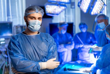 Cerrahi ekip operasyon için hazırlanıyor. Bir erkek cerrah, ekibi ameliyata hazırlanırken kendine güvenerek ameliyathanede duruyor..