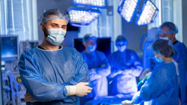 Cerrah ameliyata hazırlanıyor. Tıbbi ekip bir ameliyathanede çalışıyor. Parlak cerrahi ışıklar altında hassasiyet ve bakım sağlıyorlar..