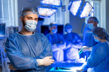 Tıbbi ekip ameliyathaneye. Meslektaşları aydınlık bir odada cerrahi bir prosedüre hazırlanırken bir tıp uzmanı ayakta duruyor..