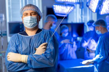 Cerrah ameliyathanede hazır. Kendine güvenen bir cerrah ameliyathanede durur. Ekip arka plandayken ameliyata hazırdır..