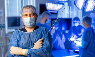 Cerrah ameliyata hazır. Önlük ve maske takan bir cerrah, modern bir ameliyathanede yapılacak cerrahi müdahaleye özgüvenli bir şekilde ayakta duruyor..