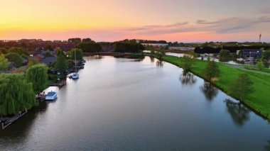 Hollanda 'nın sakin nehir manzarasının üzerinde gün batımı. Hollanda 'da sakin bir nehir yemyeşil ve küçük teknelerle çevrili renkli günbatımını yansıtır..