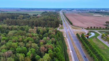 Tarımsal alan boyunca modern otoyol ve derin ahşap. İnsansız hava aracı büyük bir şehirden uzaklaşıyor..