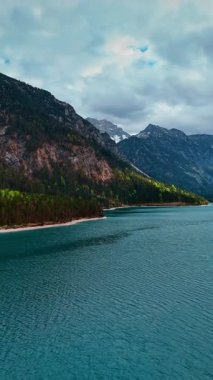 Plansee Gölü 'nün mavi su manzarası. Resimli dağların arasında. Yağmur bulutları Reutte Bölgesi 'nin yukarısında, Tyrol, Avusturya' da gökyüzünde birikti. Havadan bakış açısı. Dikey video.