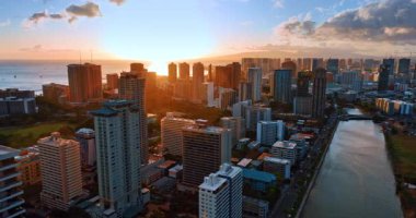 Batan güneş ışınlarında lüks Waikiki tatil köyü. Ala Wai Kanalı üzerinde İHA uçuşu. Şehrin üzerinde bulutlar.