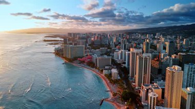 Dalgalar Waikiki, Honolulu, Hawaii, ABD sahillerine doğru akar. İnsanlar sahilde dinlenir ve okyanusta yüzer. Gri bulutlar şehrin üzerindedir. Gün batımı görüntüleri. Üst görünüm.