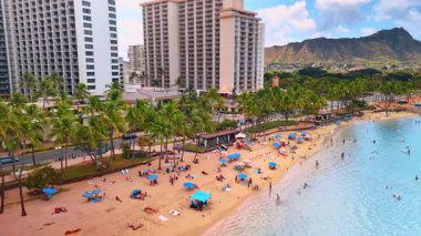 Palmiye ağaçları ve sayısız tatilcisi olan sakin kumlu bir sahil. Waikiki, Honolulu, Hawaii, ABD 'de. Diamond Head Krateri arka planda. Hava perspektifi.