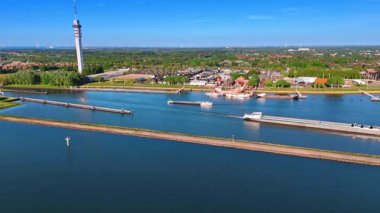 Mavnalar baraj boyunca göl kıyısında hareket ediyor. Hollanda, Lelystad 'ın manzarası. Telekom kulesi ve Batavialand Müzesi 'ne bak.
