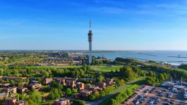 Hollanda, Lelystad 'daki telekom kulesine daha yakın uçuyor. Güneşli bir günde yeşil şehrin manzarasına hava perspektifi. Arkaplanda barajlar olan Merkemeer Gölü.