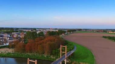 Kanal üzerindeki köprü Hollanda 'da bir kasabaya giden yola çıkıyor. Gün batımında rahat bir yerleşim yeri. Hava perspektifi.
