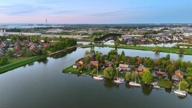 Ayna yüzeyi olan kanallar konut evlerinin etrafını sarar. Yatlar ve tekneler küçük rıhtımların yanında duruyor. Gün batımında Hollanda kırsalında. Hava perspektifi.
