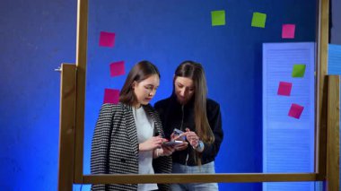 Uzun saçlı beyaz kadınlar akıllı telefona odaklanmış gözüküyorlar. Kadınlar internetten bilgi arar ya da kontrol eder. Cam tahta kadınların önünde..