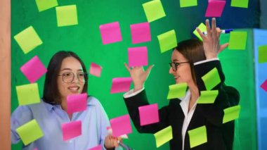 Güzel esmer, beyaz kadınlar cam duvarın arkasında dikiliyorlar. Kadınlar tahtadaki çıkartmaları alır ve geri atar..